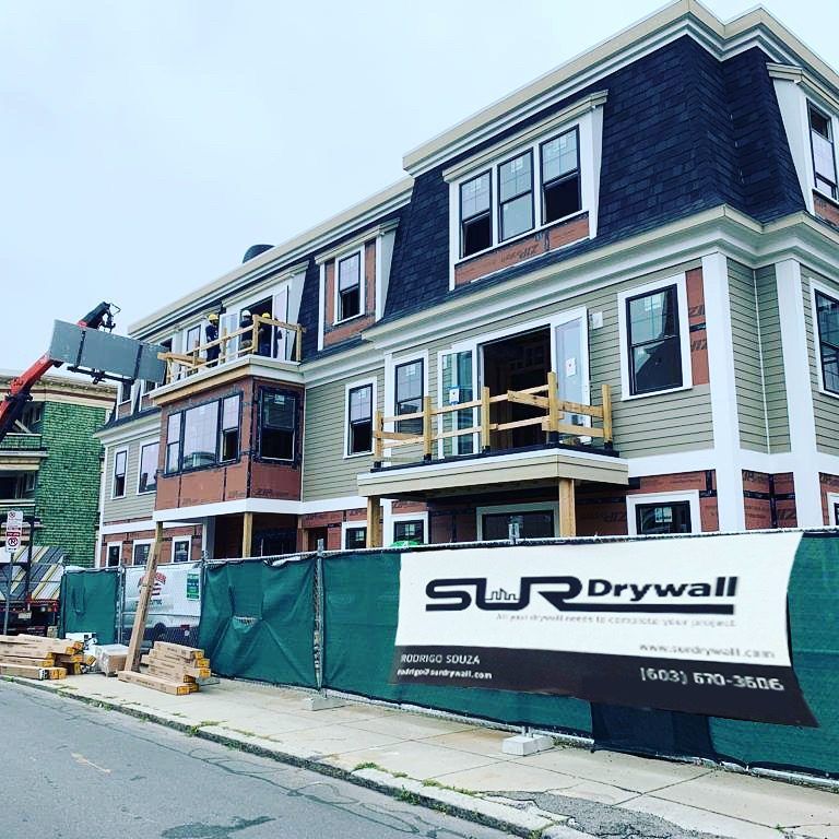 Multifamily building under construction with a SUR Drywall banner on the site fence